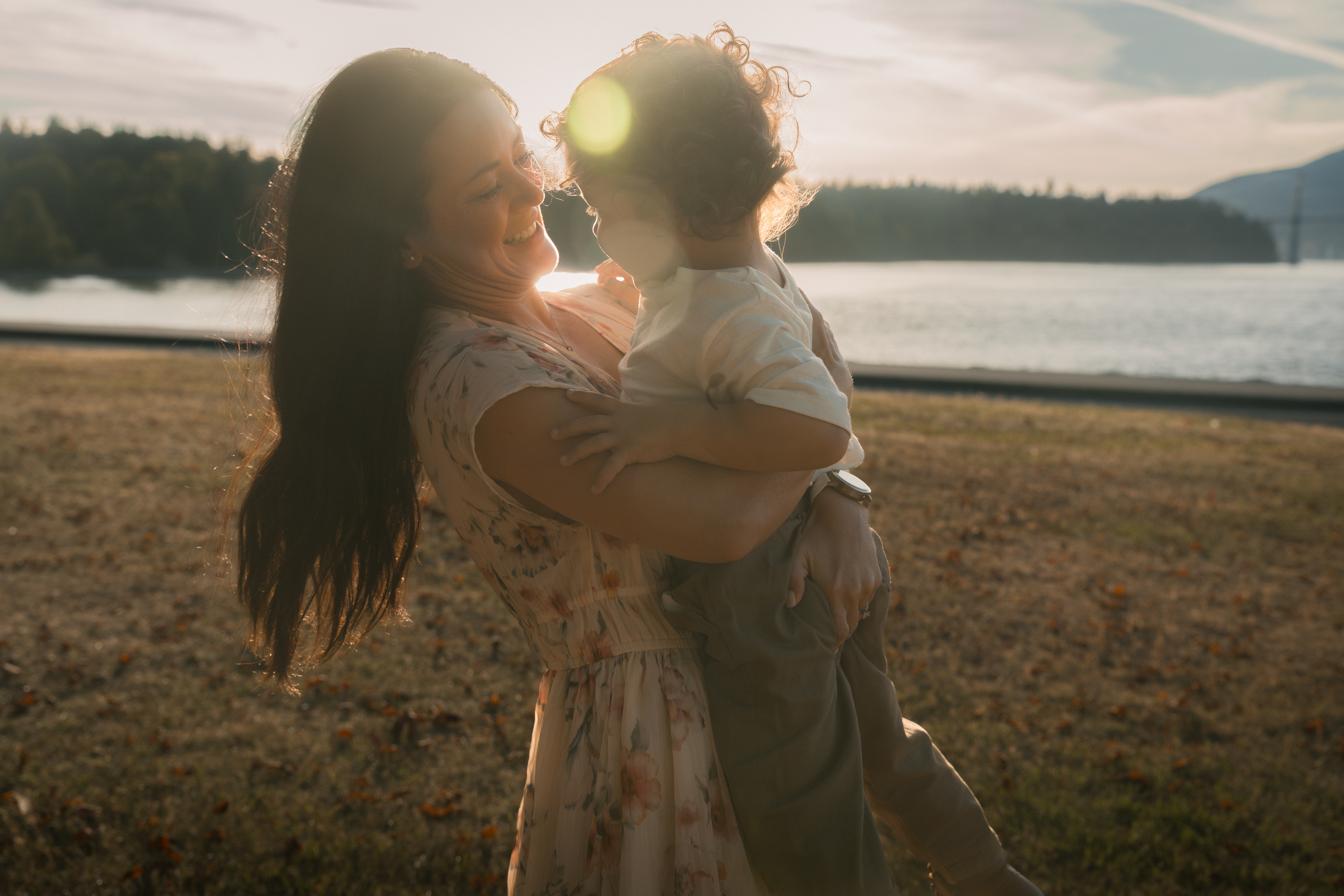 A mother holding her child in the last warm light beside the water