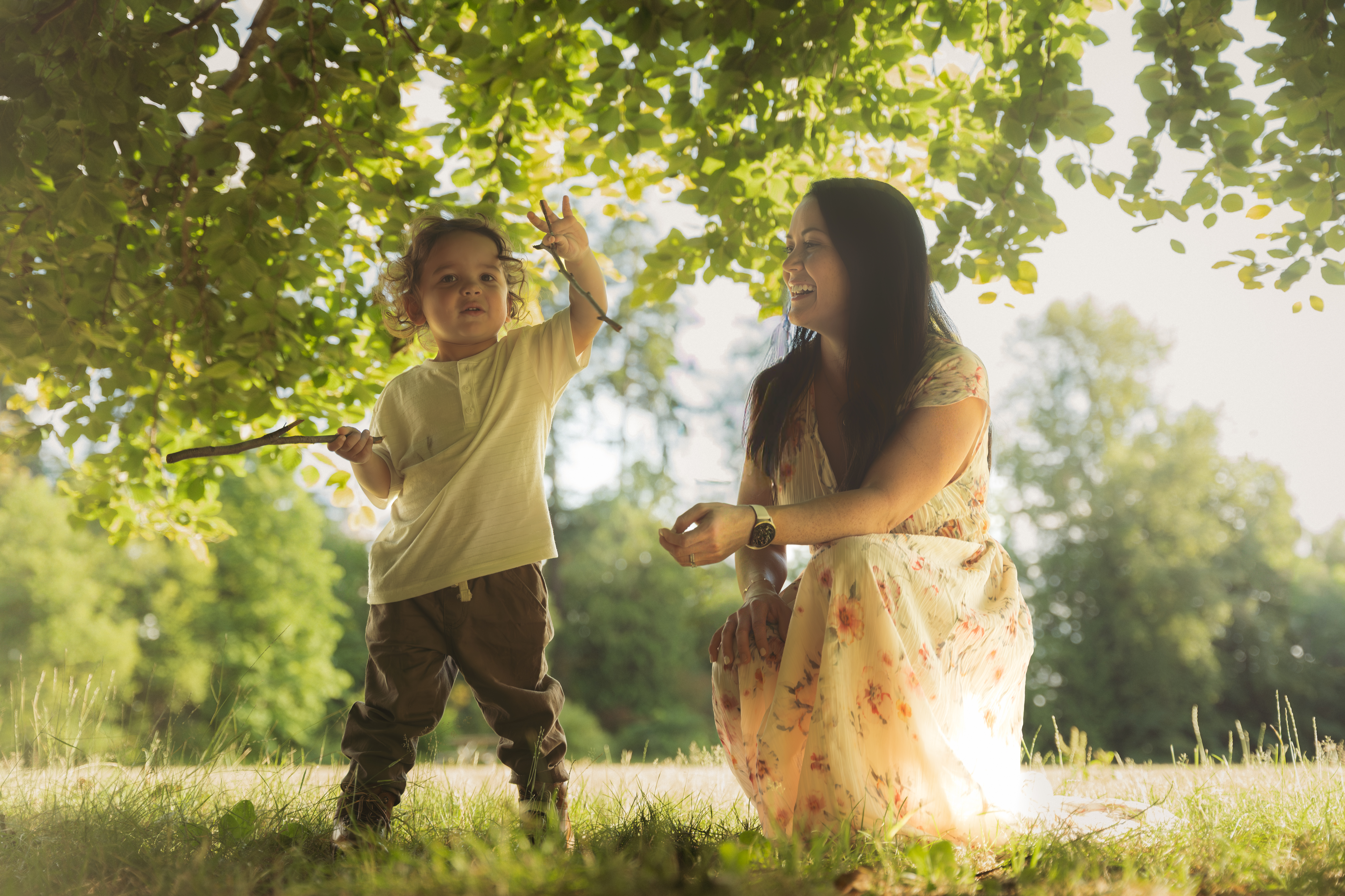 A mother and child playing beneath sunlit leaves