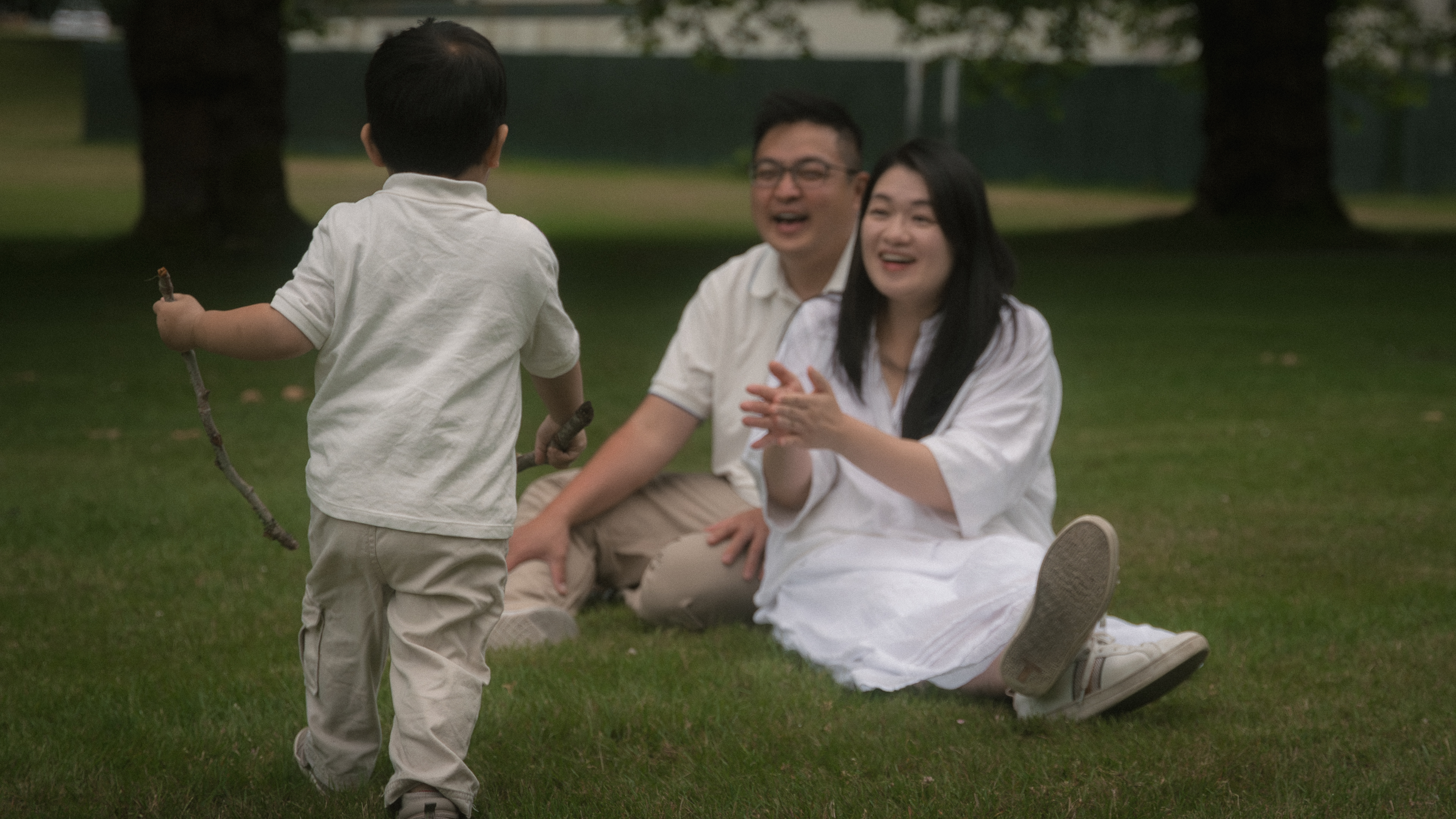 A young child running toward smiling parents seated on the grass