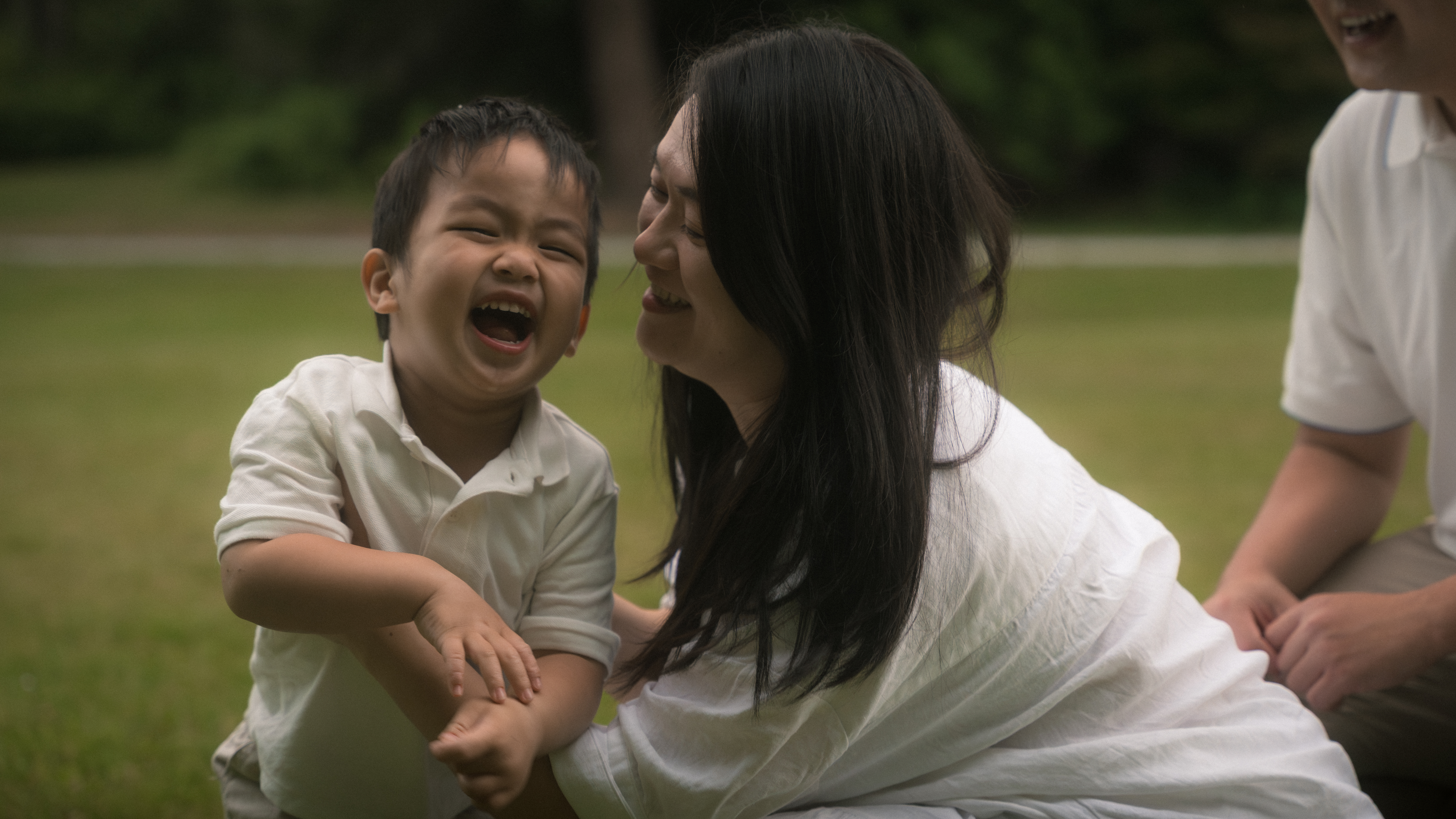 A mother and young child laughing together in the grass
